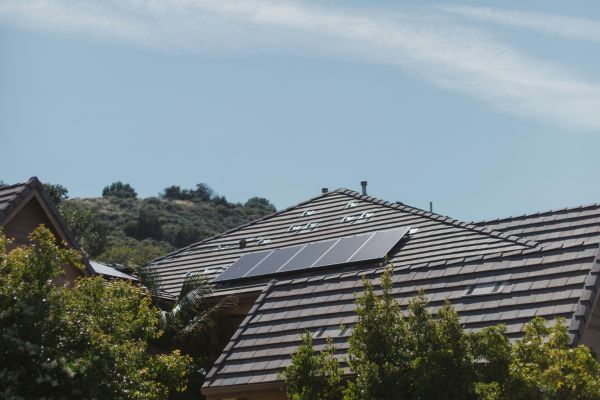 Haus mit dunkel gedecktem Dach, auf dem mehrere Solarpaneele installiert sind, umgeben von Bäumen und Garten.